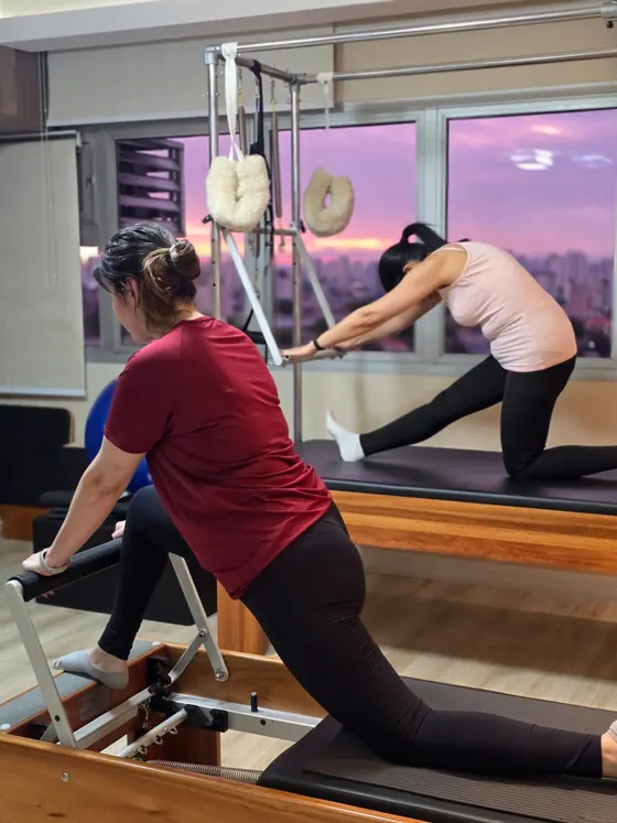 Aula de pilates no reformer com a cidade ao entardecer